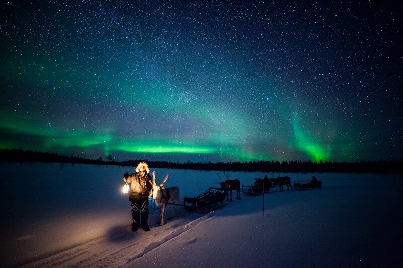 Man met lantaarn en husky's onder het noorderlicht in Ruka, Fins Lapland