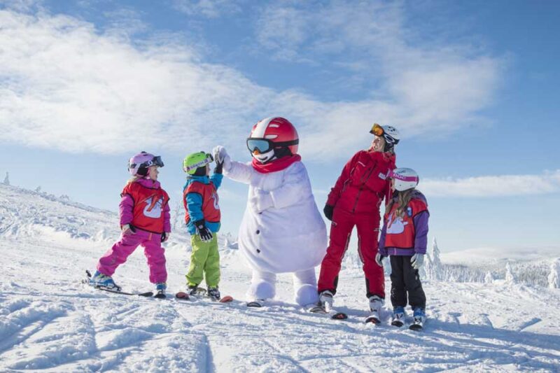 Drie kinderen krijgen tijdens de skiles een high five van Valle, de mascotte van Sälen in Zweden