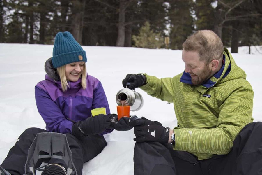 Twee wandelaars schenken chocolademelk in tijdens een sneeuwschoenwandeling in Canada