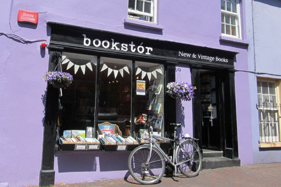 Een grijze fiets leunend tegen een paarse gevel van een boekenwinkel in Cork