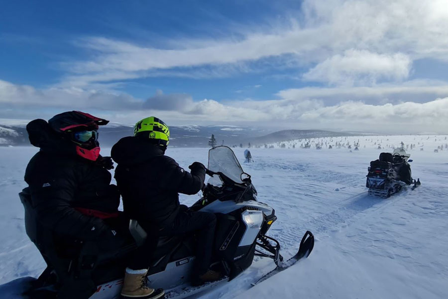 Twee mensen zitten op een sneeuwscooter bovenop een besneeuwde berg bij Fulufjellet