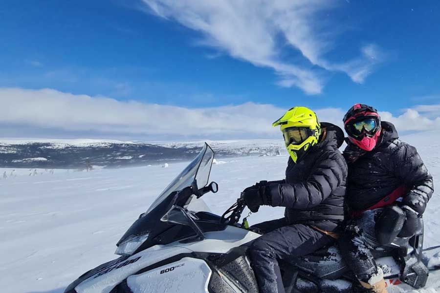 Twee mensen zitten op een sneeuwscooter bovenop een besneeuwde berg bij Fulufjellet