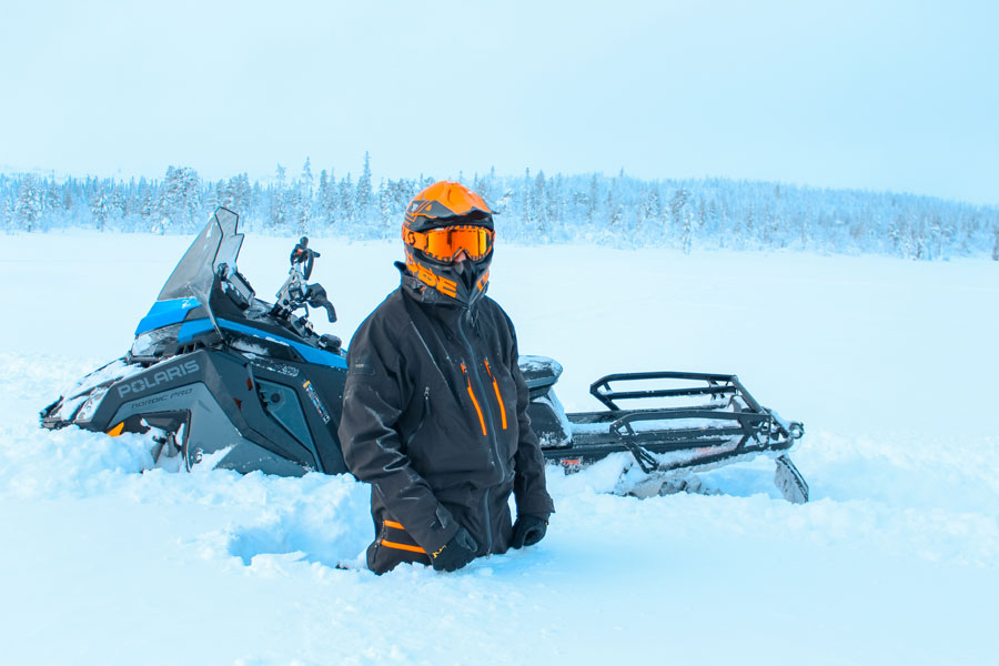 Man staat tot zijn knieën in de sneeuw naast zijn sneeuwscooter, Villa Fregn